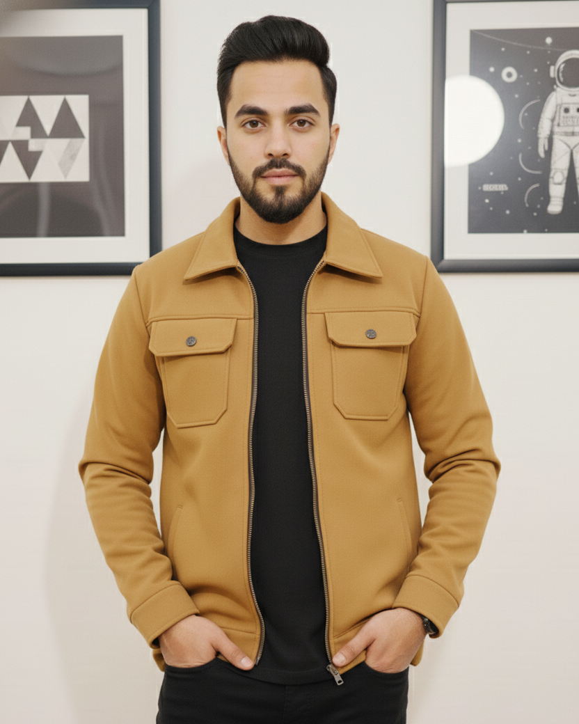 Man wearing a tan jacket over a black shirt in a room with framed pictures on the wall.